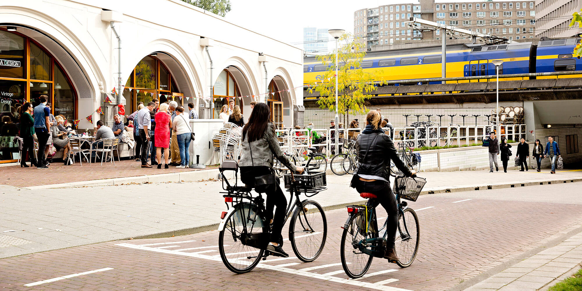 Vrouwen fietsen voorbij Hofbogen waar mensen staan.